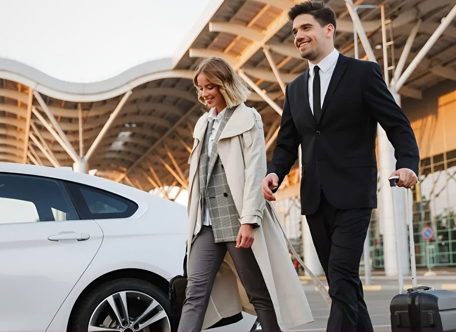 A man and woman walk with luggage beside a white car outside a modern airport terminal.